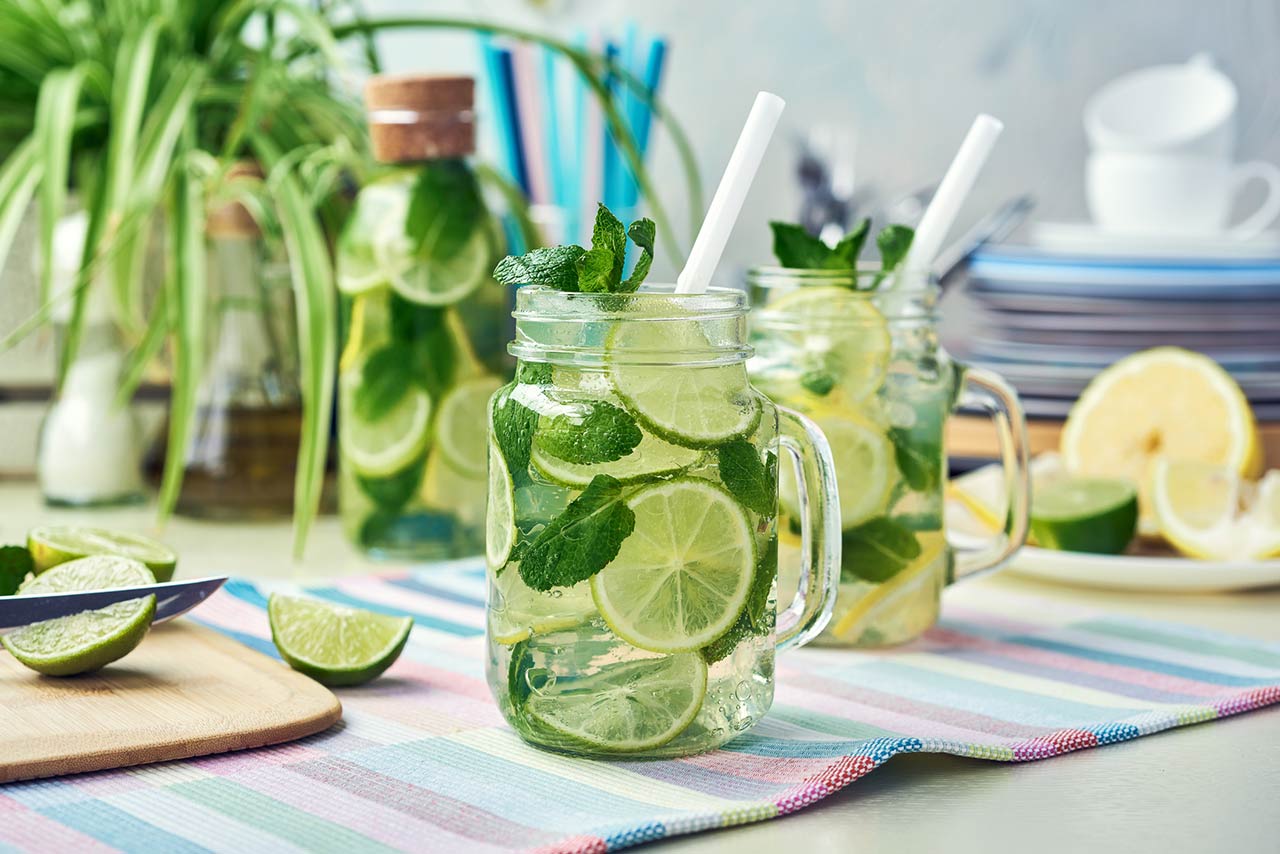 Two glasses and a bottle of homemade lemon, lime, and mint lemonade sit on the wooden dining table