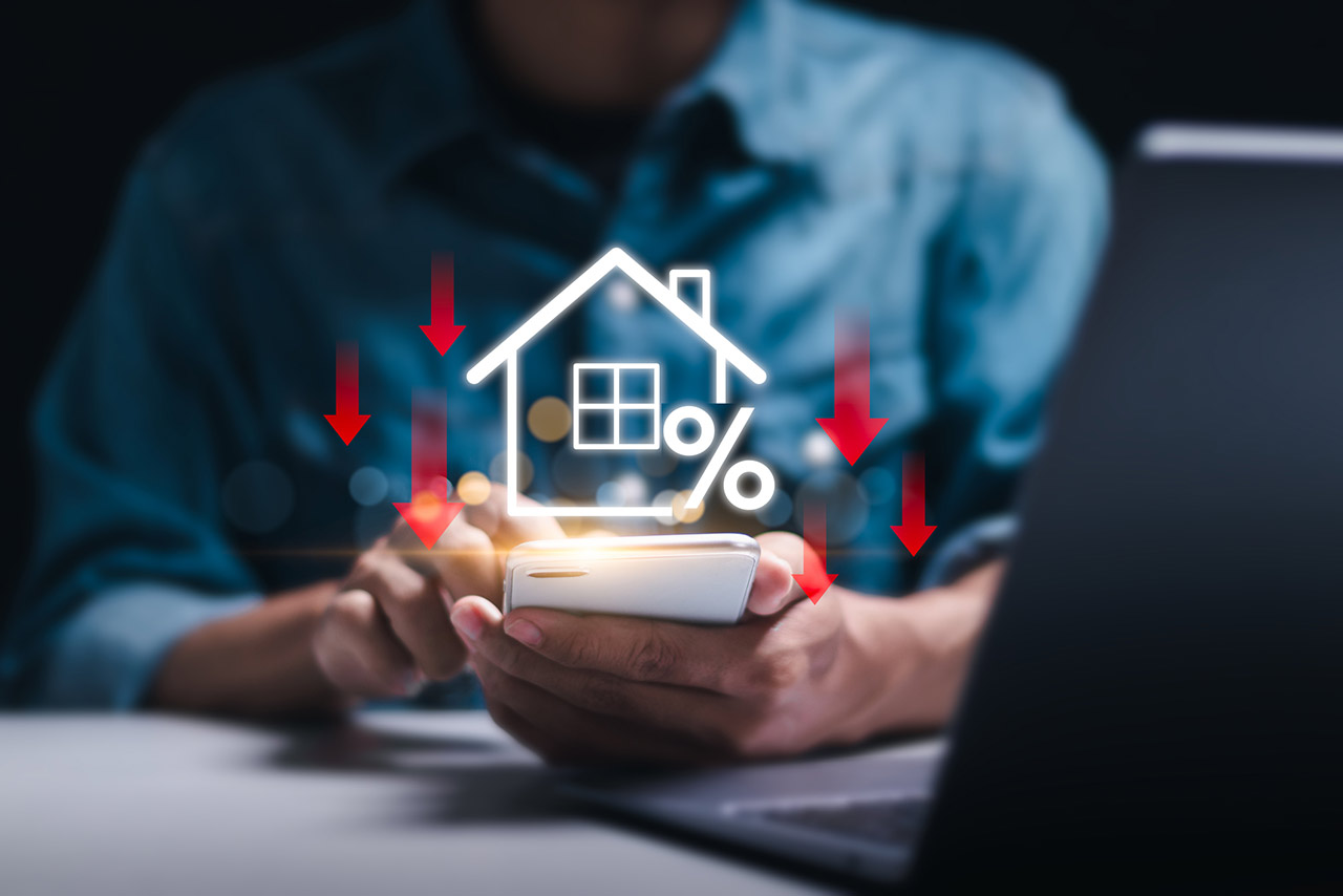 Businessman use smartphone with virtual home icon and down arrow for economical real estate and lower mortgage interest rates